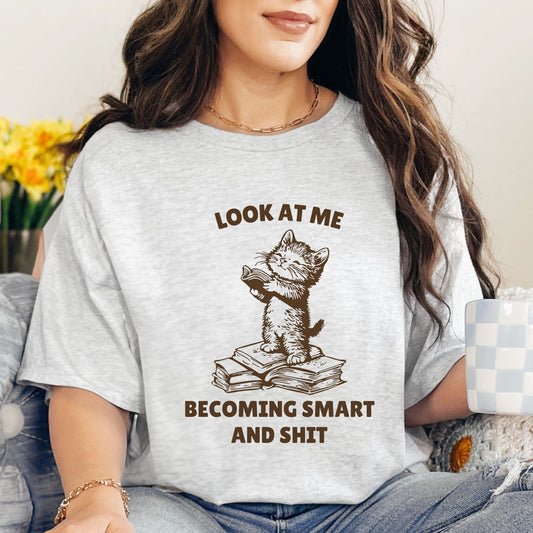 Humorous Cat Reading T-Shirt – 'Look at Me Becoming Smart and Sh*t' – Unisex Graphic Tee for Book Lovers-Ash-Family-Gift-Planet